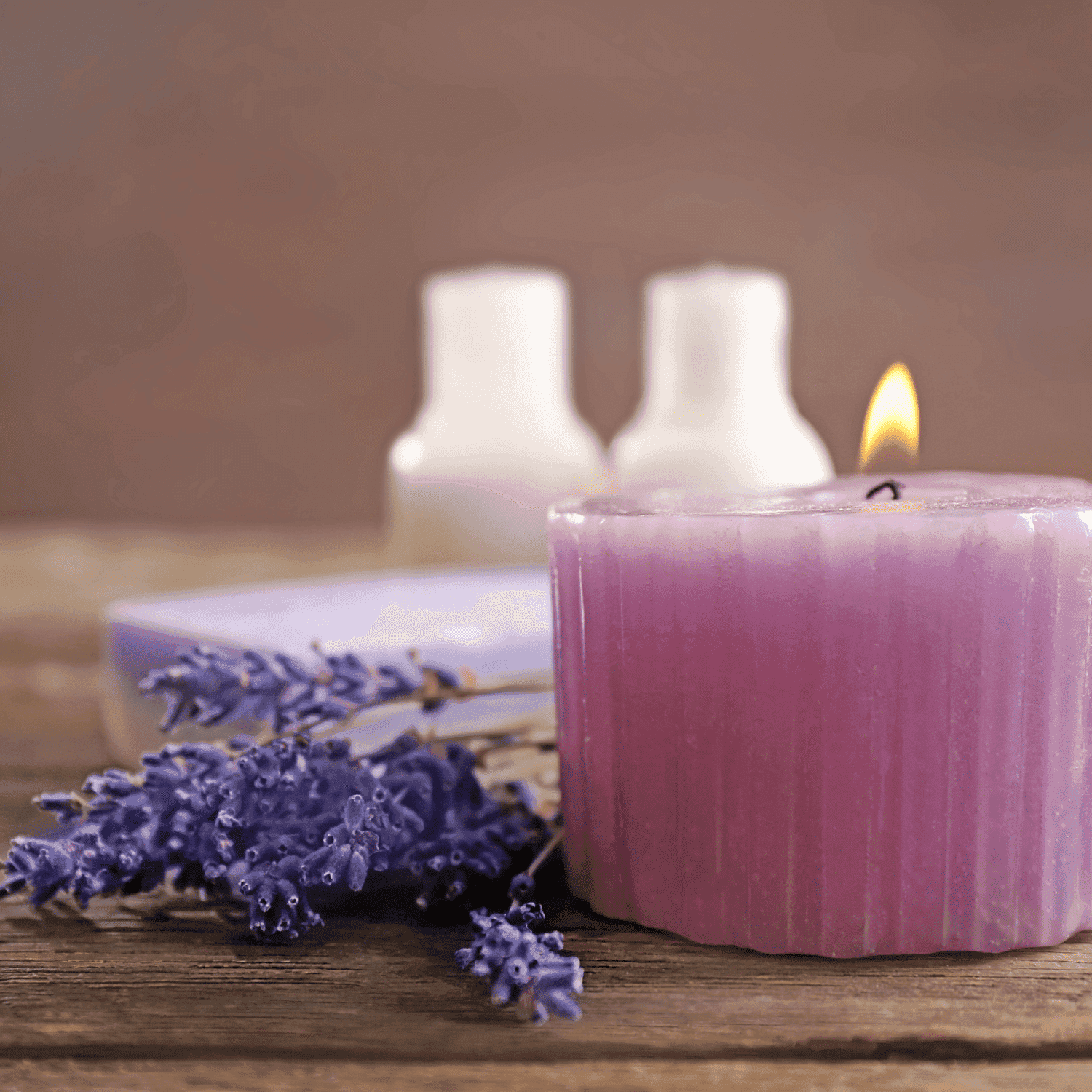 Purple candle and lavender with two bottles on rustic wooden table.