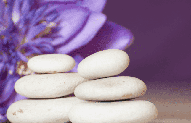 Stack of smooth white stones with a purple flower in the background.