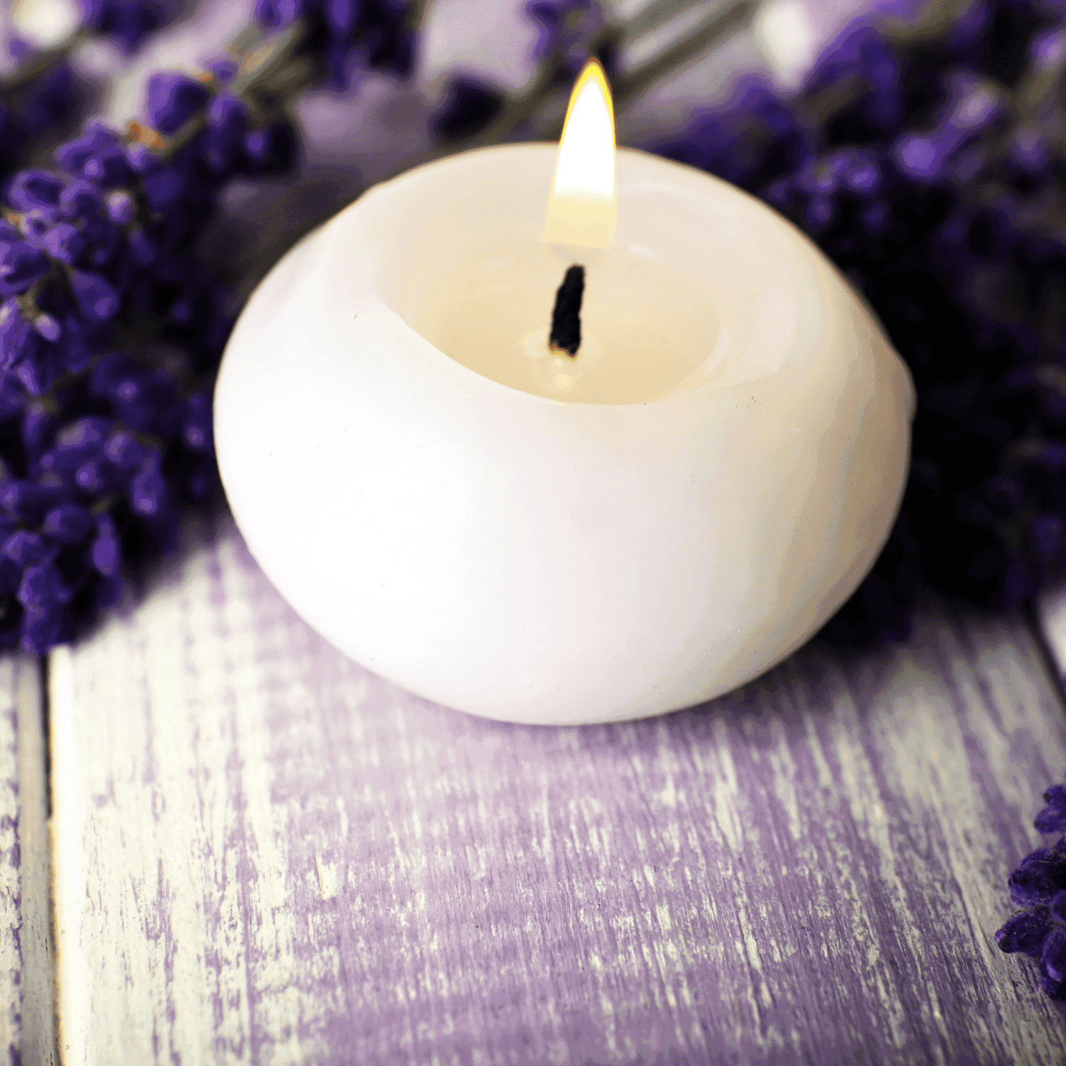White candle lit among lavender flowers on rustic wooden surface.